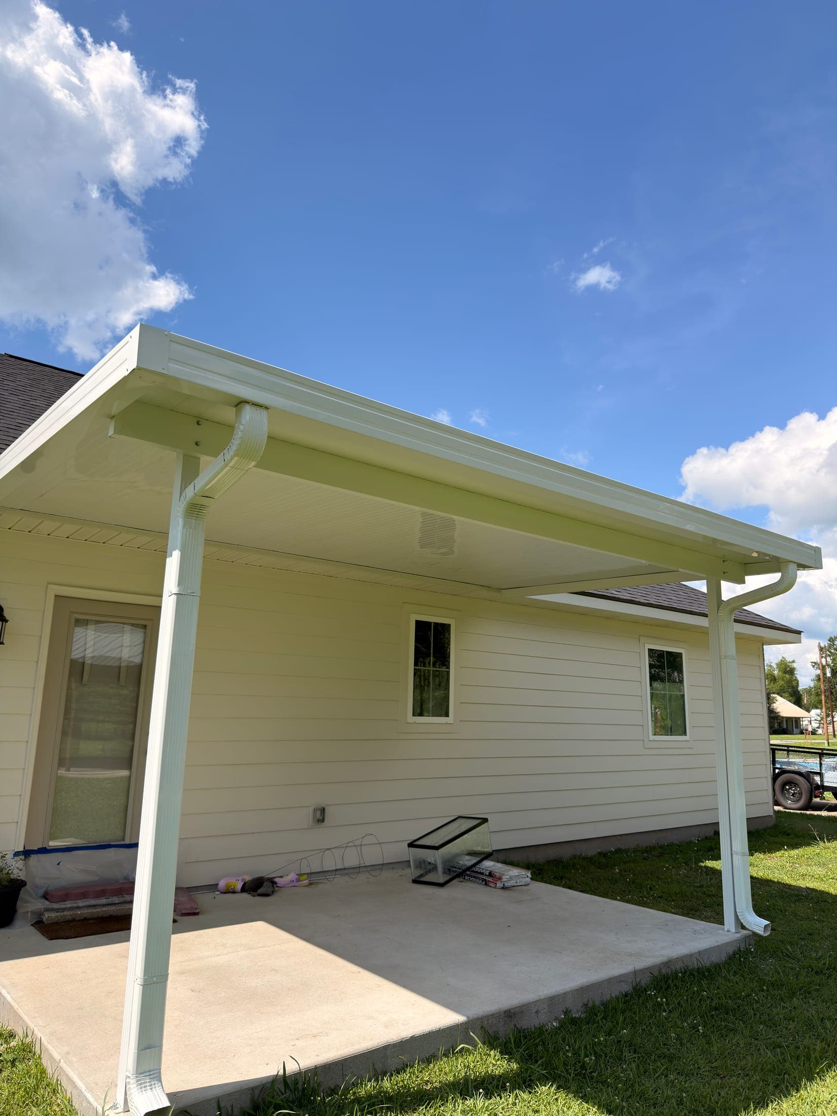 White aluminum patio cover on posts over a concrete patio behind a cream-sided home