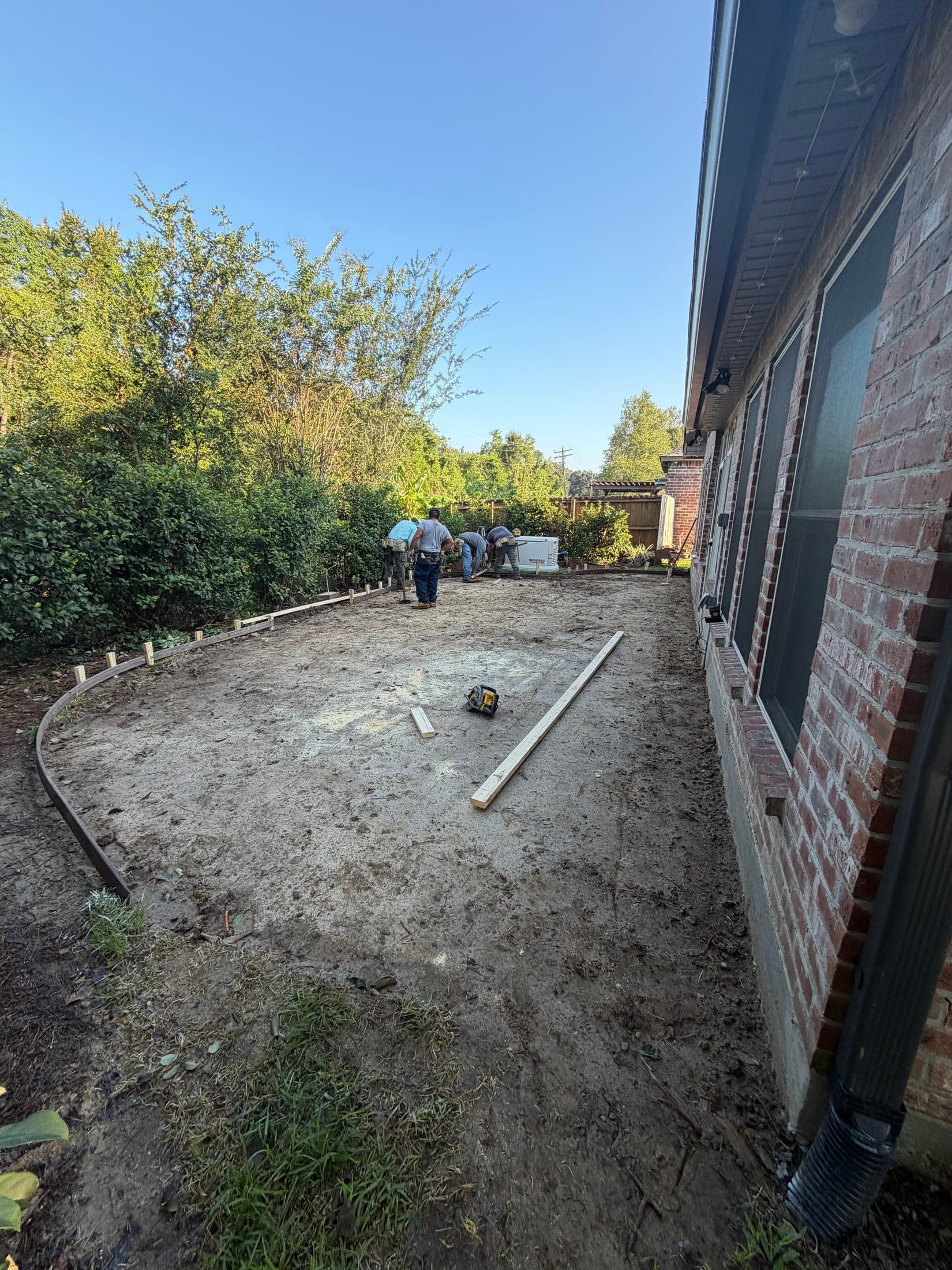Curved wood forms staked on a graded base beside a brick home before a patio pour
