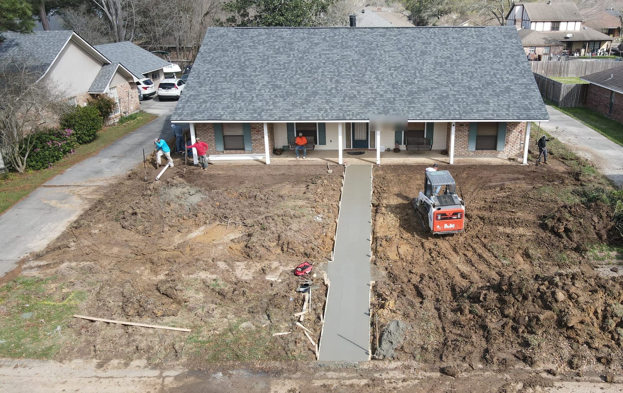 Drone view of a fresh concrete front walk running from the street to the porch while the crew grades the yard