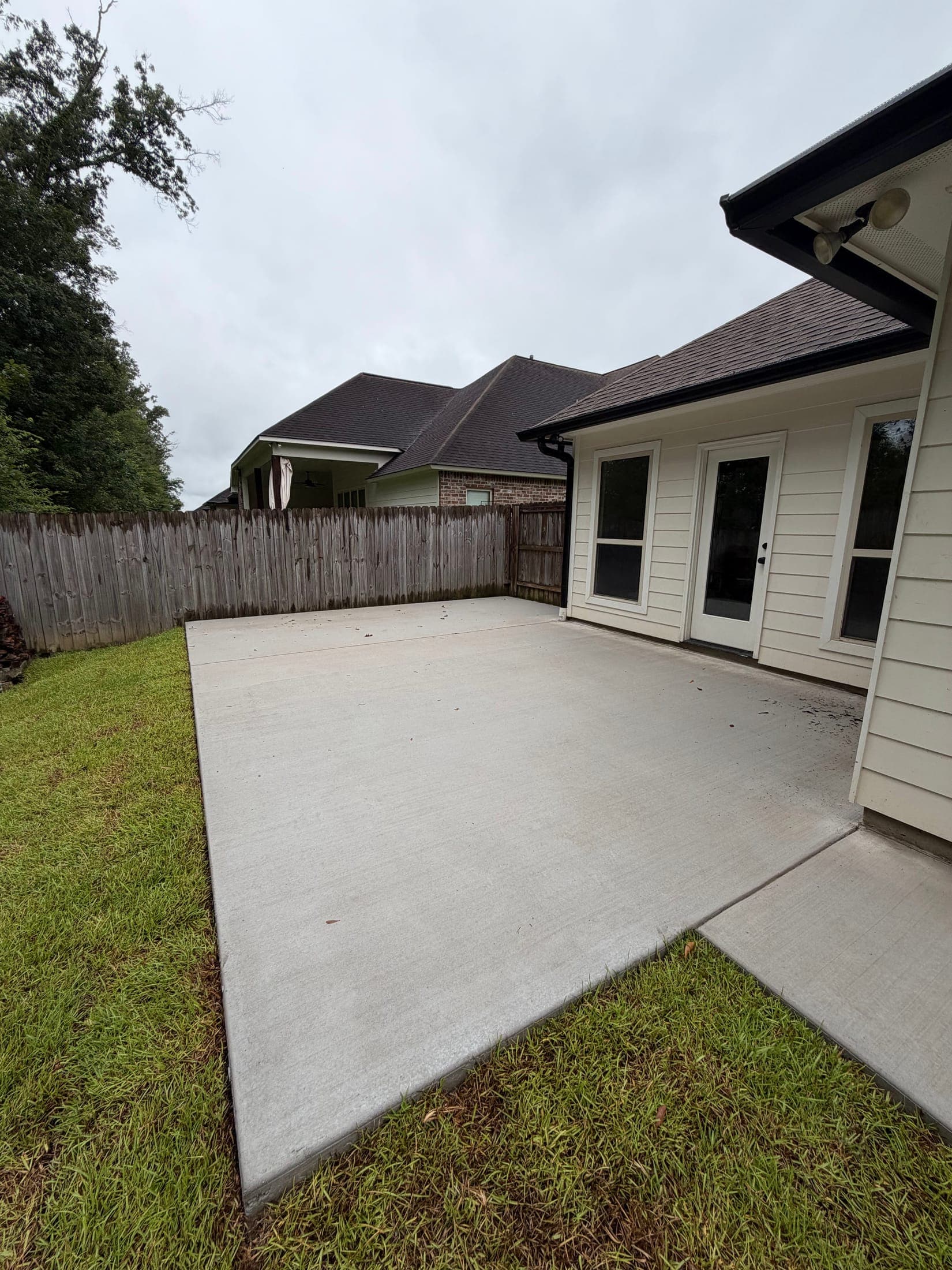 Fresh concrete patio extending from the back doors of a cream-sided house toward the lawn