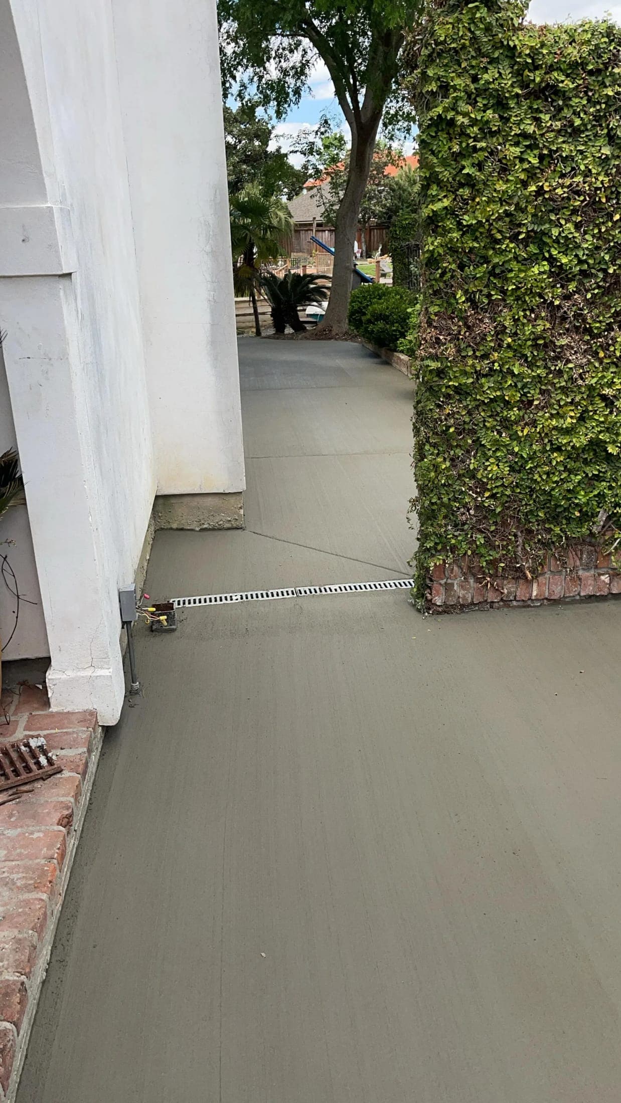 New concrete walkway beside a white stucco wall with a trench drain set across it